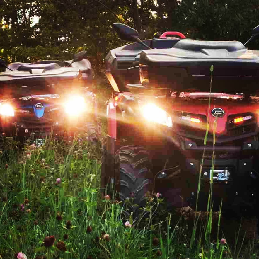 Deux VTTs avec phares puissants allumés dans un champ au coucher du soleil